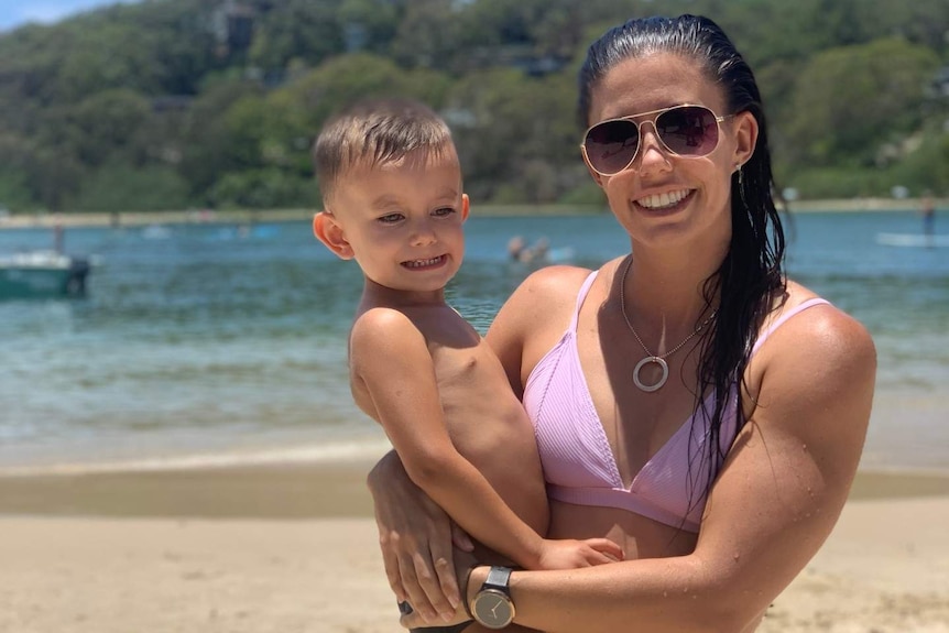 A woman hugs her son on a beach.