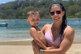 A woman hugs her son on a beach.