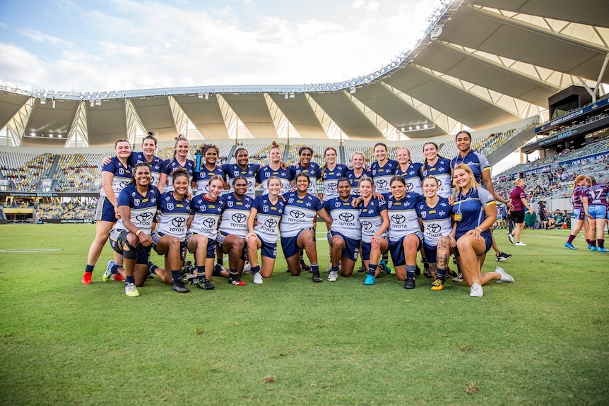 A women's rugby league team poses inside a large stadium