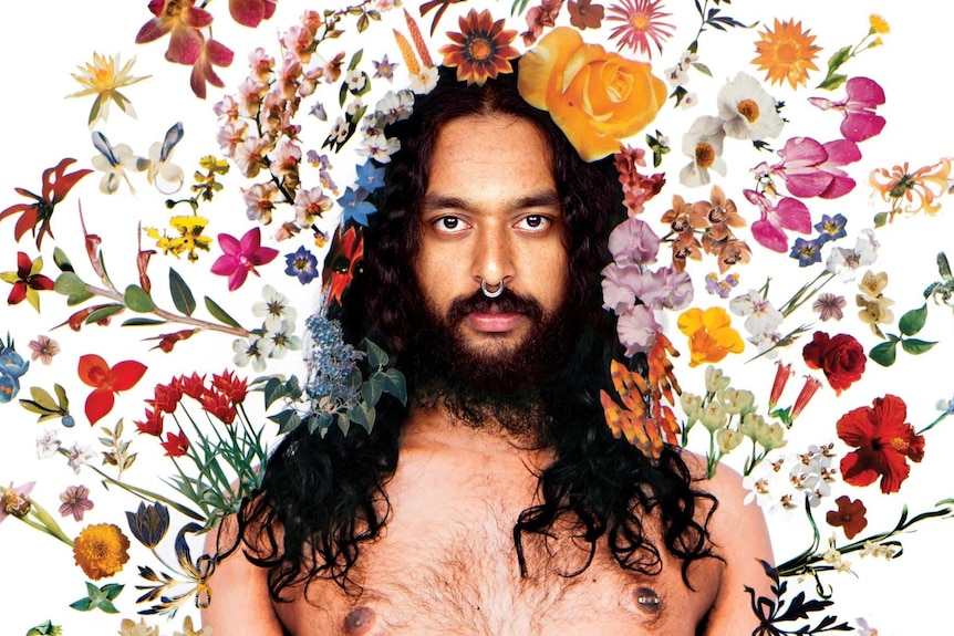 A portrait of artist Ramesh Mario Nithiyendran, standing shirtless inside an aura of flowers.