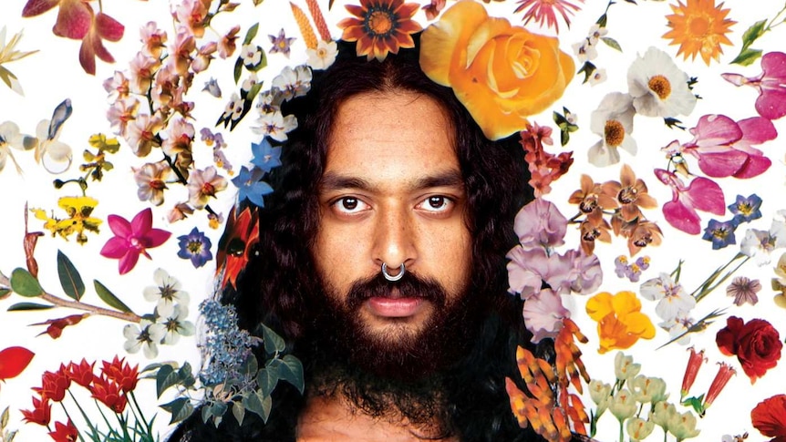 A portrait of artist Ramesh Mario Nithiyendran, standing shirtless inside an aura of flowers.