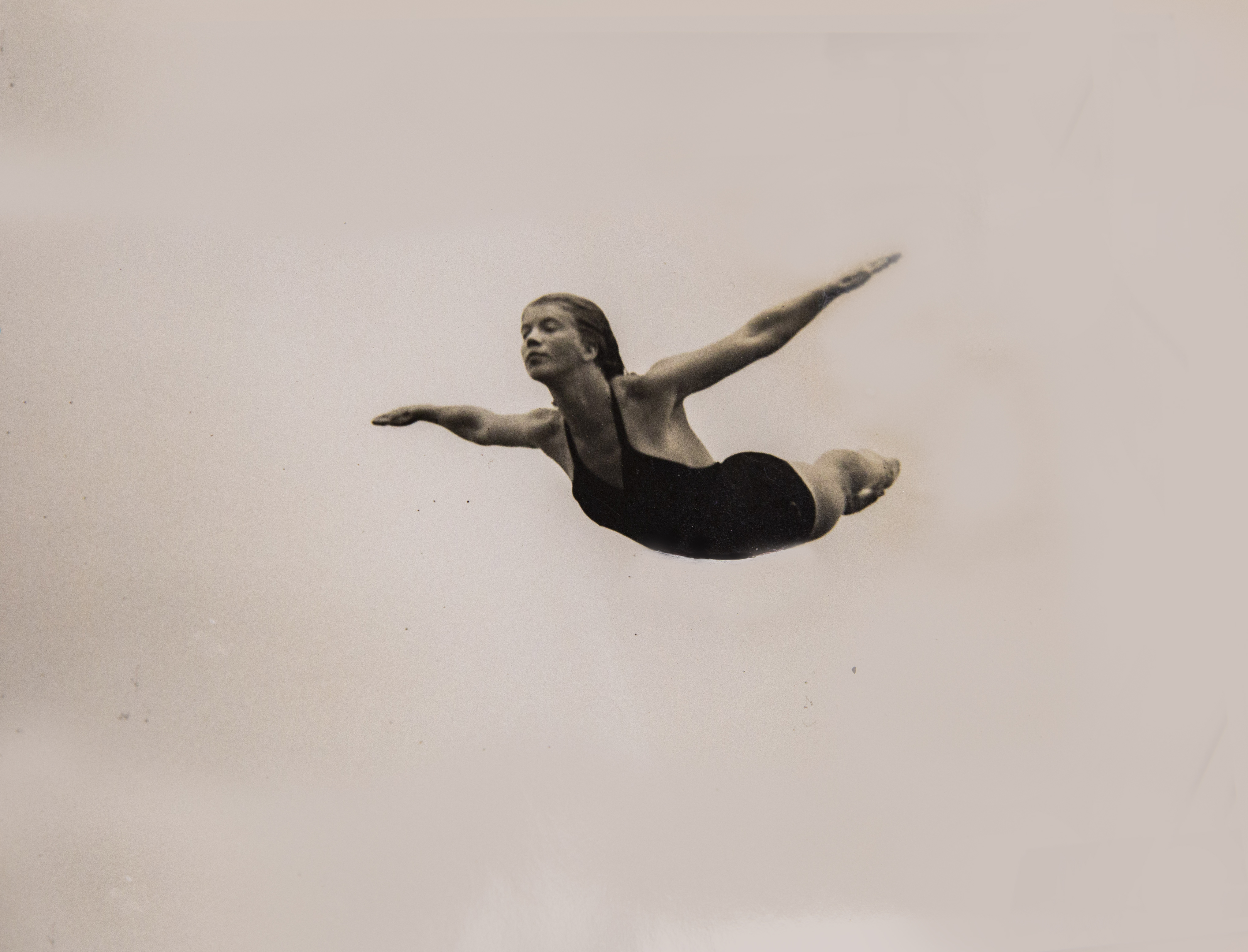 An old photo of a young woman diving through the air into a pool