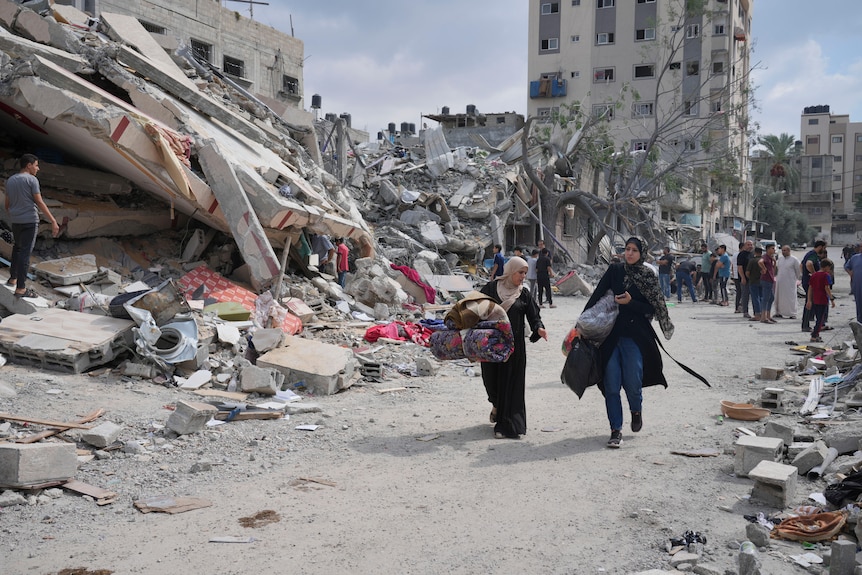 Palestinian women walk by buildings destroyed in Israeli airstrikes.