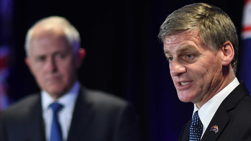 Australian PM Malcolm Turnbull looks on as NZ counterpart Bill English speaks at a lectern.