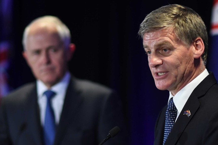 Australian PM Malcolm Turnbull looks on as NZ counterpart Bill English speaks at a lectern.