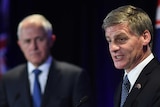 Australian PM Malcolm Turnbull looks on as NZ counterpart Bill English speaks at a lectern.