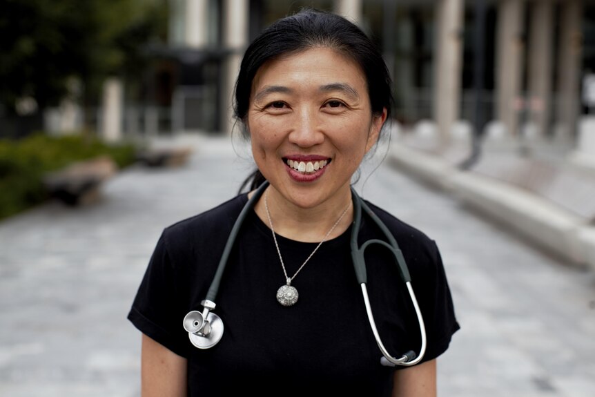 A woman with a stethoscope around her neck smiles at the camera.
