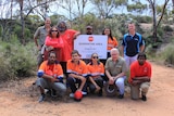 Indigenous rangers and management pose for a photo around the quarantine area sign in front of a dam
