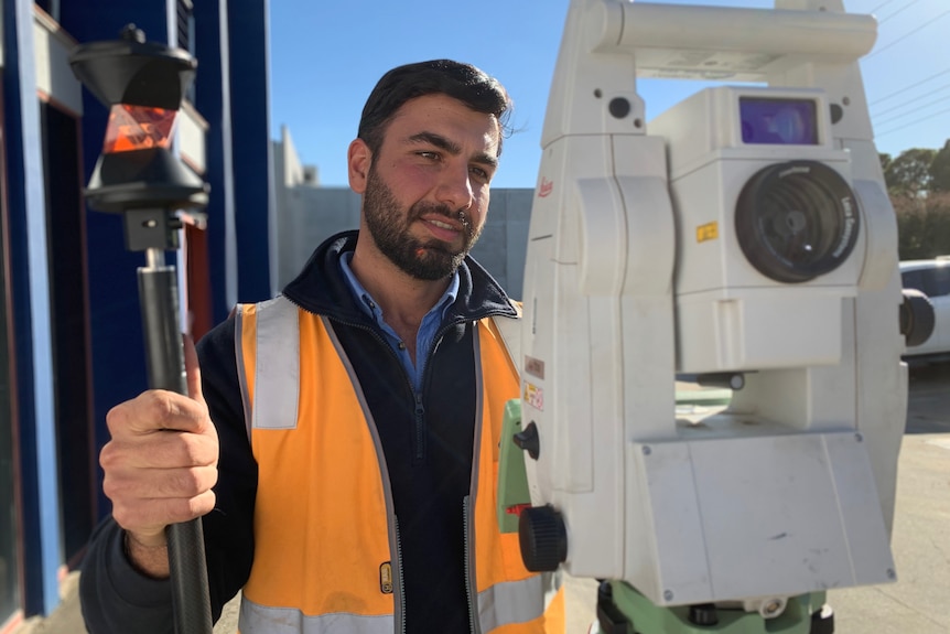 A young man holding equipment he uses to undertake engineering work.