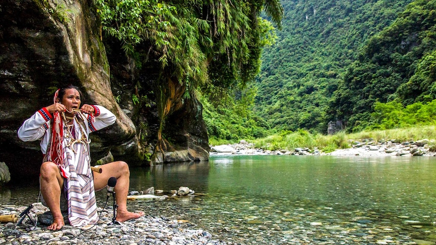 Man plays traditional instrument next to river.