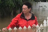 A woman stands in the front yard of her Townsville home. Floodwaters have consumed her fence.