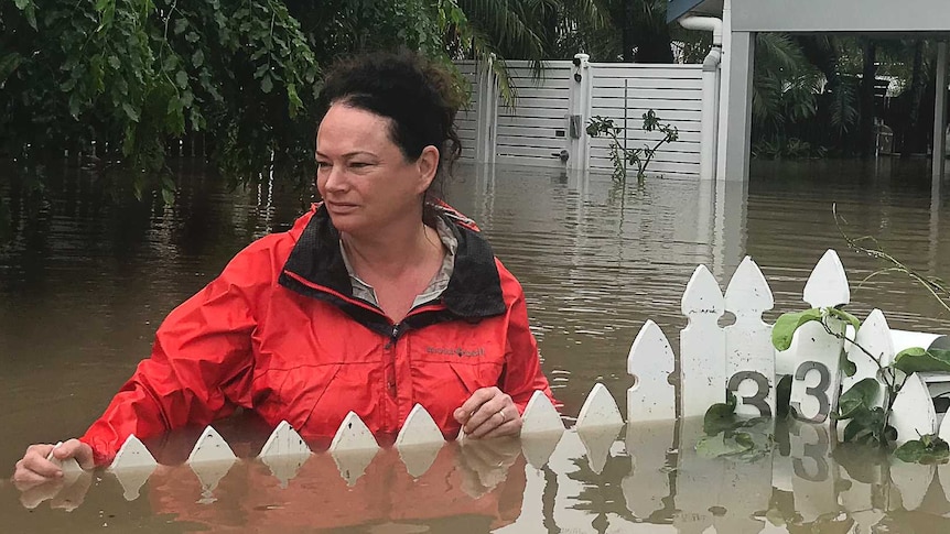 A woman stands in the front yard of her Townsville home. Floodwaters have consumed her fence.