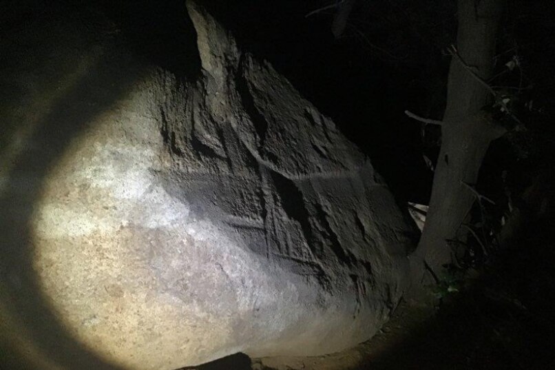 Artificial lighting casts deep shadows across a boulder, highlighting carving marks.