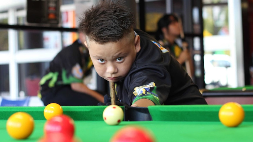A young boy with a pool cue at a pool table.