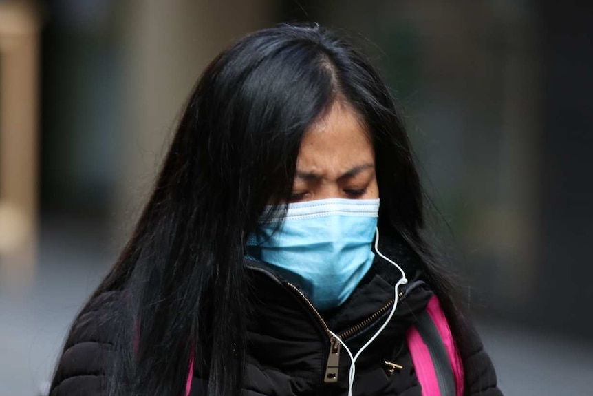 A woman wearing a mask and a winter coat looks down at her phone.