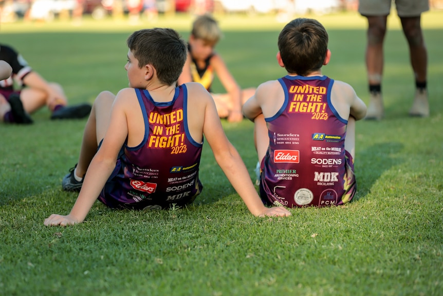 Two boys sitting on grass wearing singlets that read United in the Fight 