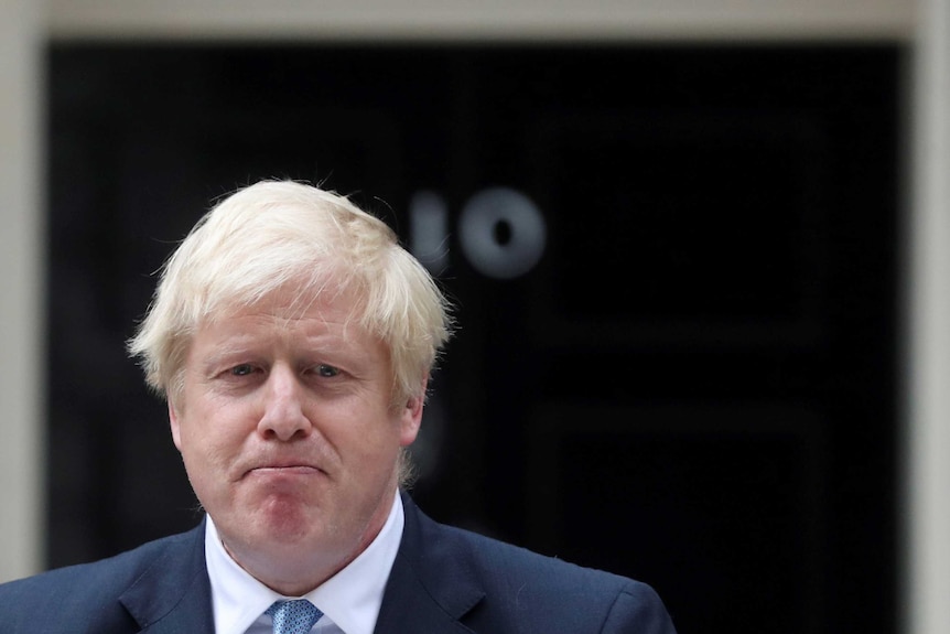 British Prime Minister Boris Johnson standing outside 10 Downing Street wearing a suit and tie looking downcast