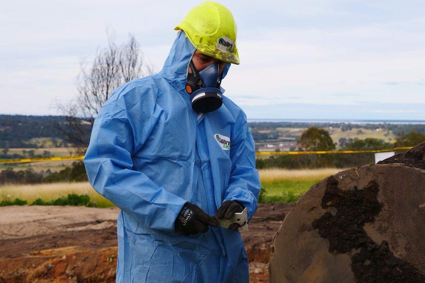 A man in a hazmat suit cleaning an excavator.