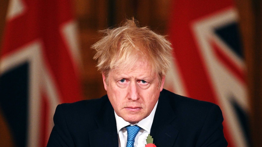 Britain's Prime Minister Boris Johnson stares forward in front of a British flag.