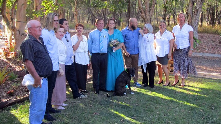 A row of people with bride and groom in the middle, with happy couple also holding a dog on the lead.
