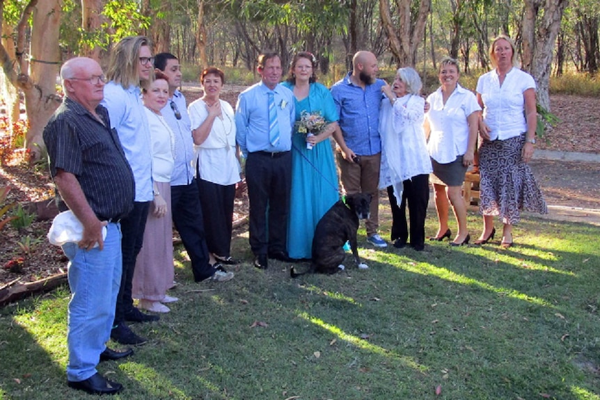 A row of people with bride and groom in the middle, with happy couple also holding a dog on the lead.