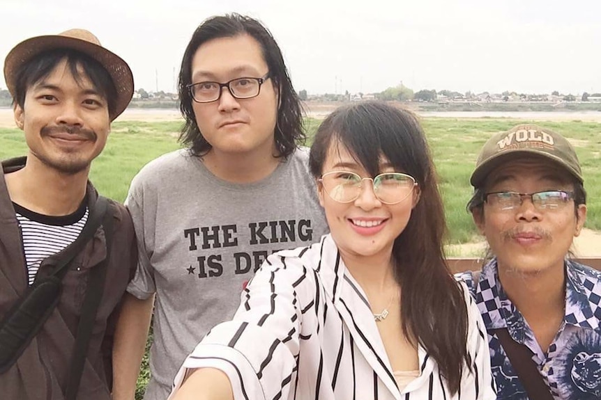 Three men and a woman stand in a grassy field near a river