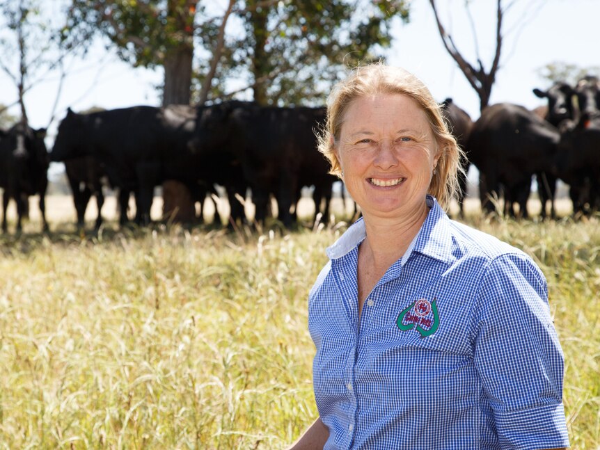 Alison stands in a paddock with a mob of black cattle behind her.