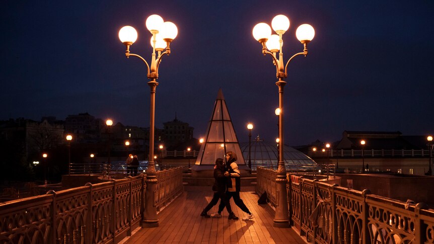 A couple with with street lights either side dances on a footbridge near the Independence Square in Kyiv