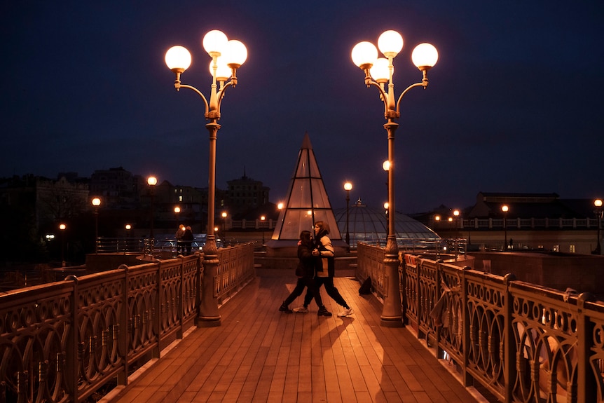 A couple with with street lights either side dances on a footbridge near the Independence Square in Kyiv