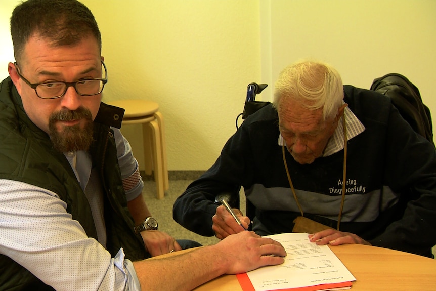 David Goodall sits with Duncan Goodall, as the older man signs papers.