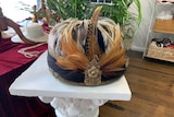 Ornate hat adorned by multi coloured feathers and gold flower broach
