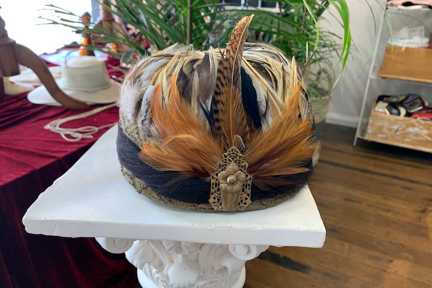 Ornate hat adorned by multi coloured feathers and gold flower broach