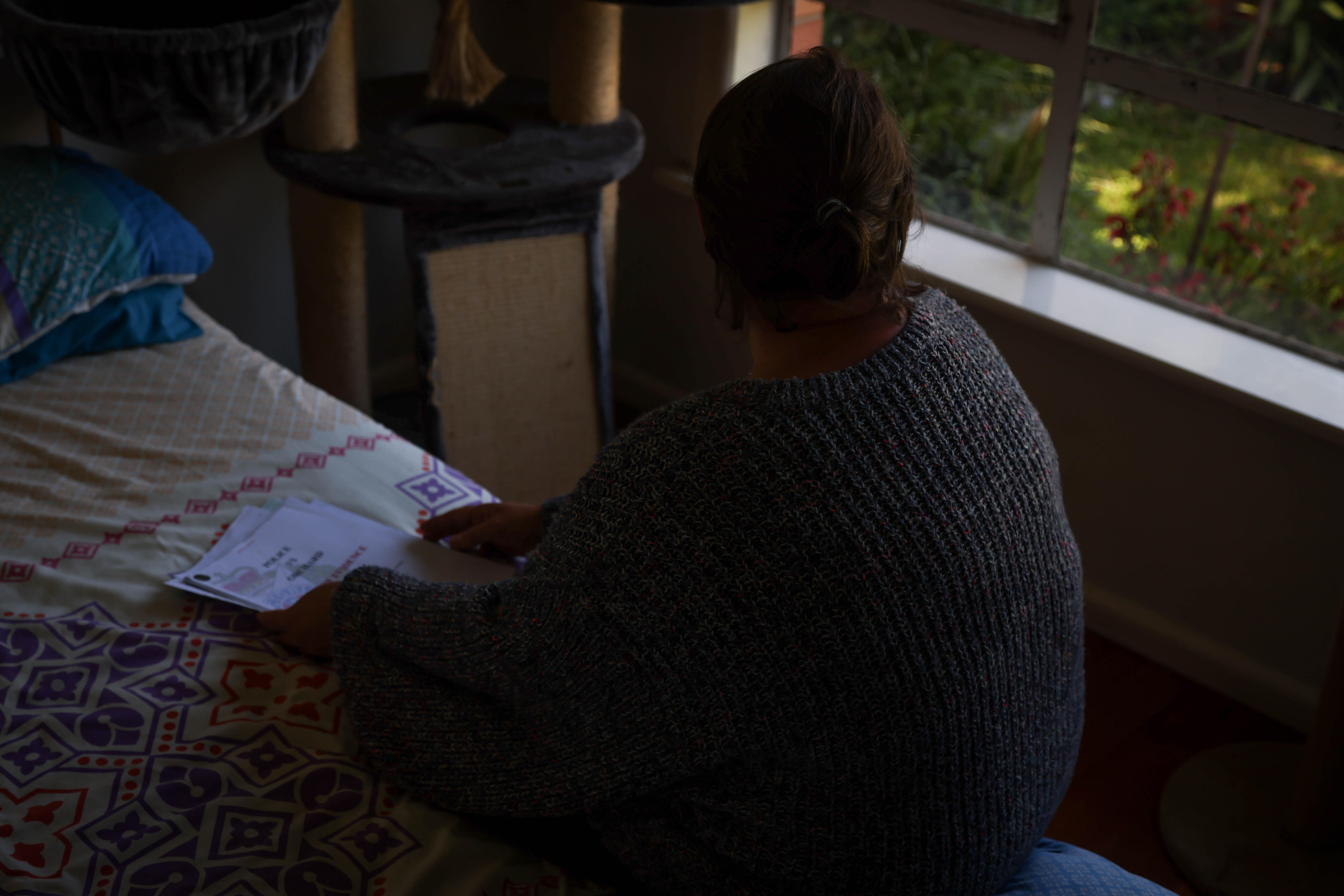 Ella sitting on the bed, looking at documents.