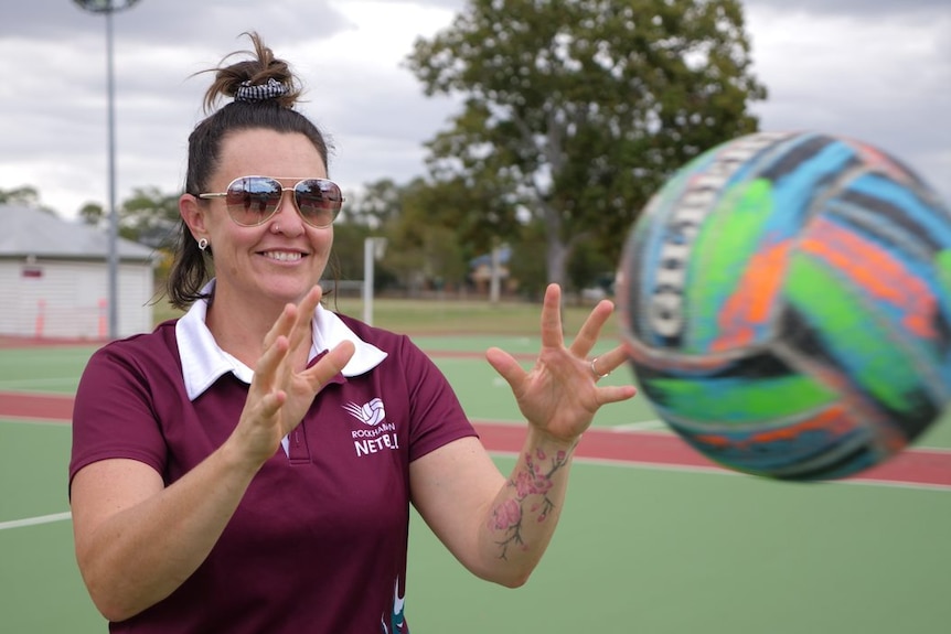 Woman with sunglasses, smiles as she catches a netball.