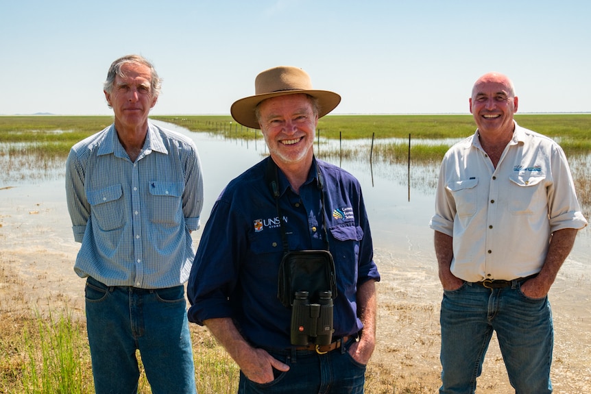 Three men standing in front of an inland lake