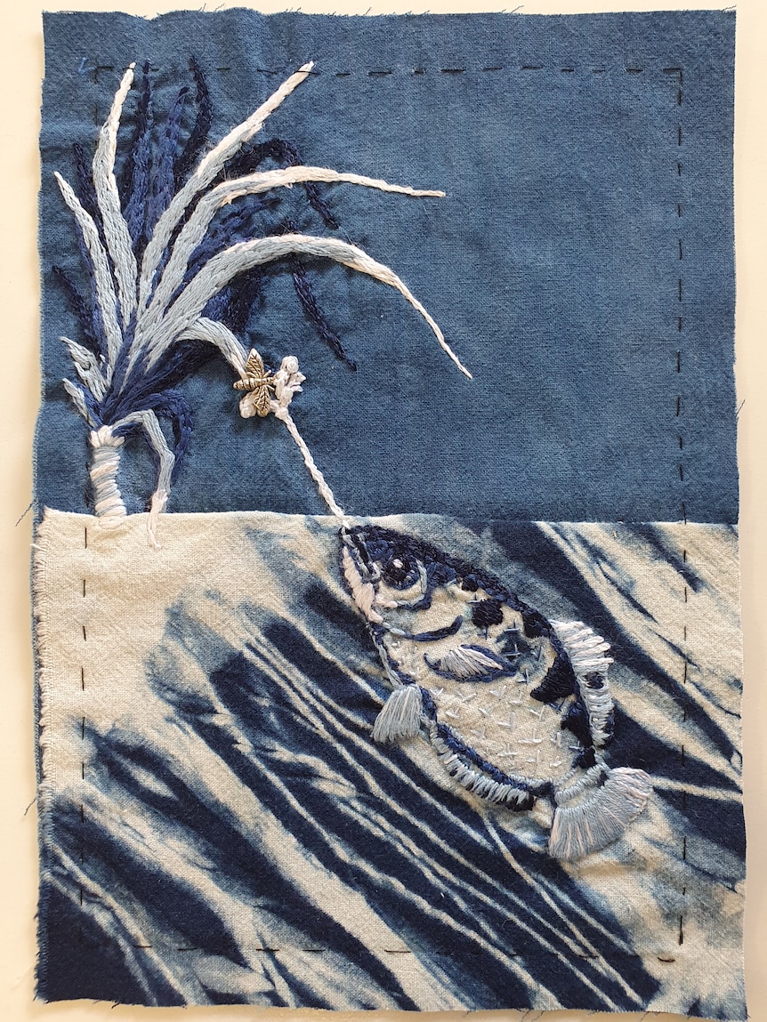 A piece of fabric with a fish and pandanus stitched into it.