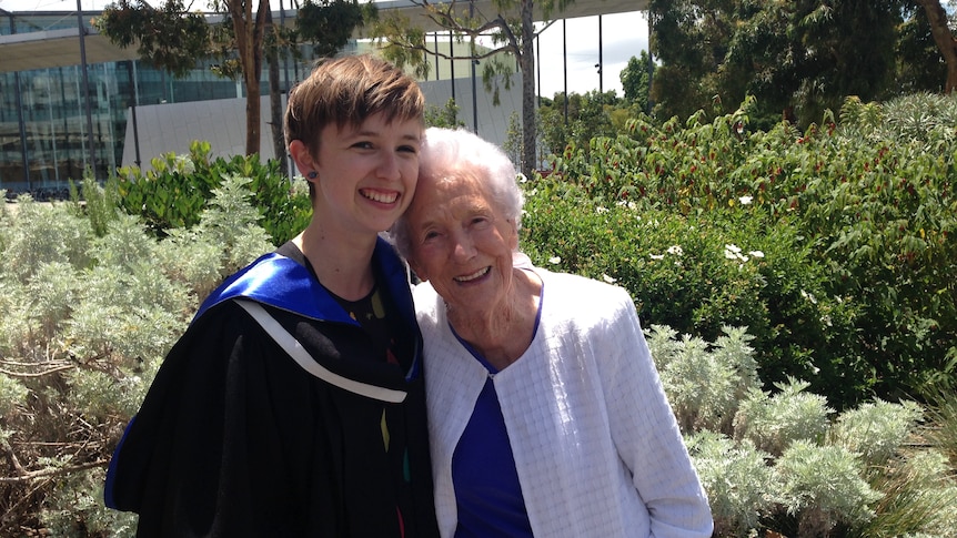 Kate Clark wearing a black graduation gown with blue collar, smiling next to an elderly woman.