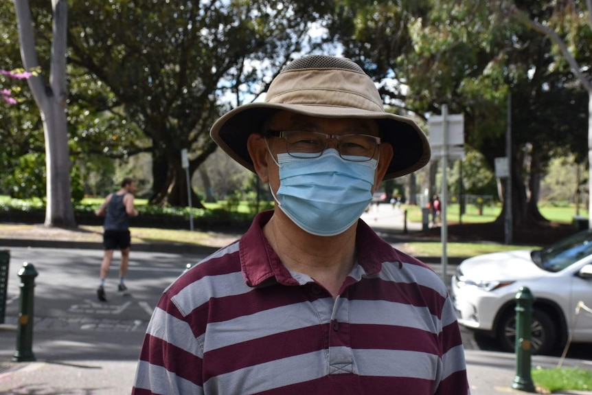 A man in a park wearing a face mask and a hat.