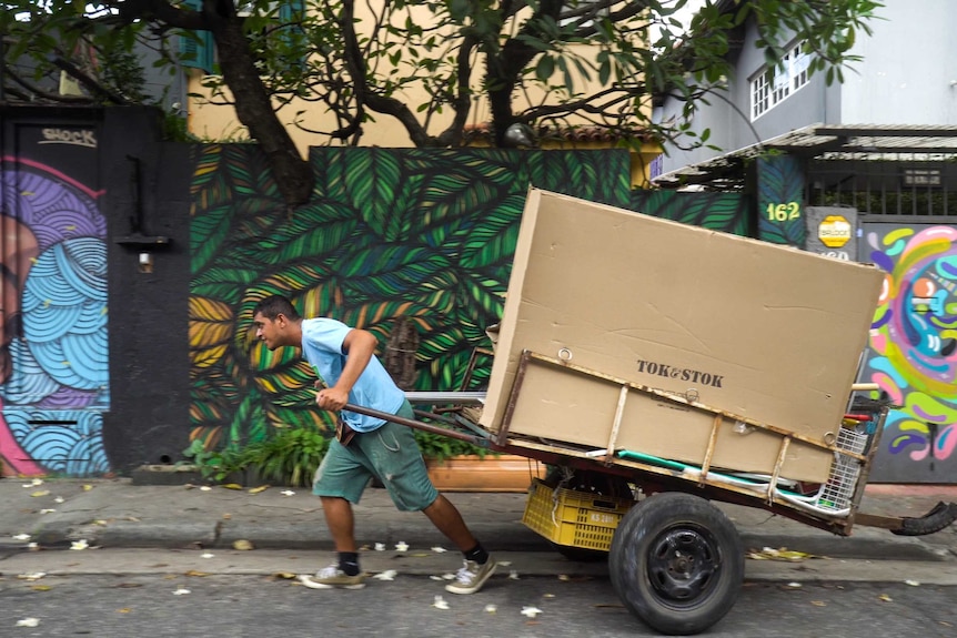 A catadore pulls his cart along a street with graffitied walls in the background.