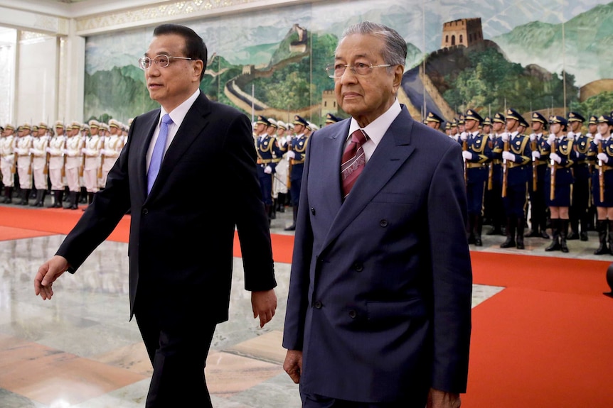 Li Keqiang and Mahathir Mohamad walk together past a guard of honour.