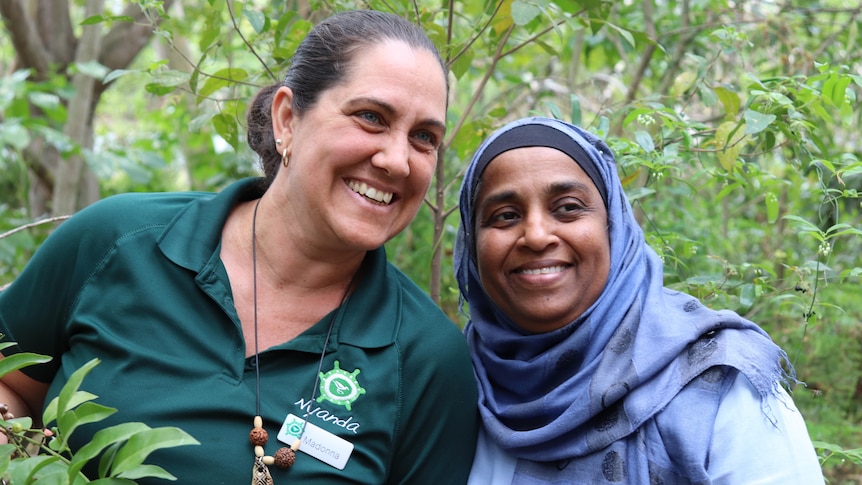 Two women standing smiling in bush land.