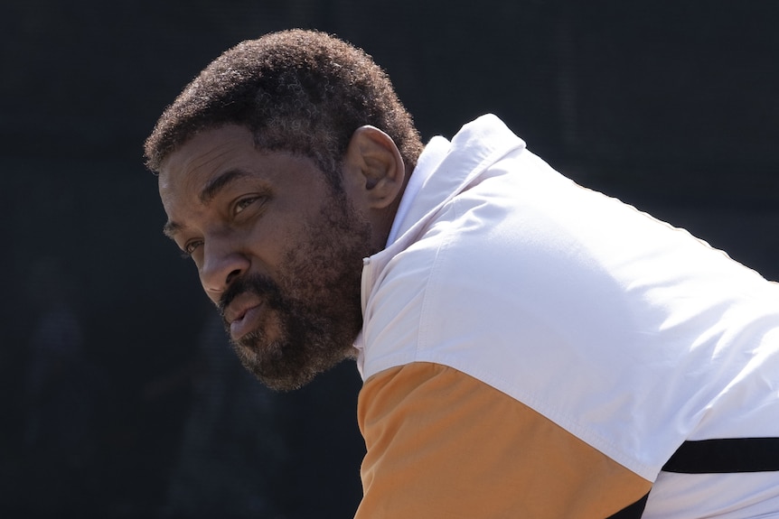 A middle-aged African American man sits wearing tennis attire, looking glum