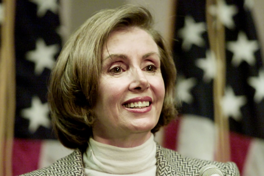 Nancy Pelosi smiles in front of an American flag 