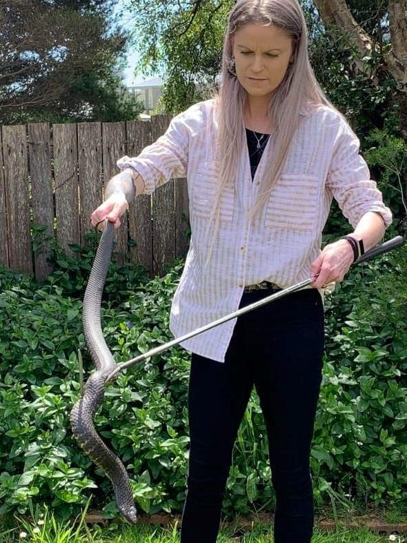 A woman holds a large snake by the tail.