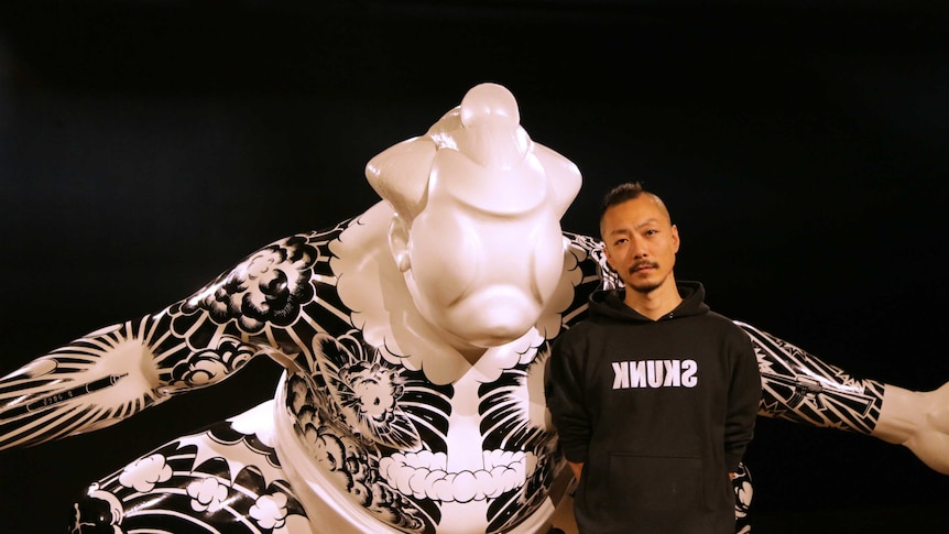 The artist poses with a larger than life sculpture of a sumo wrestler covered in tattoos