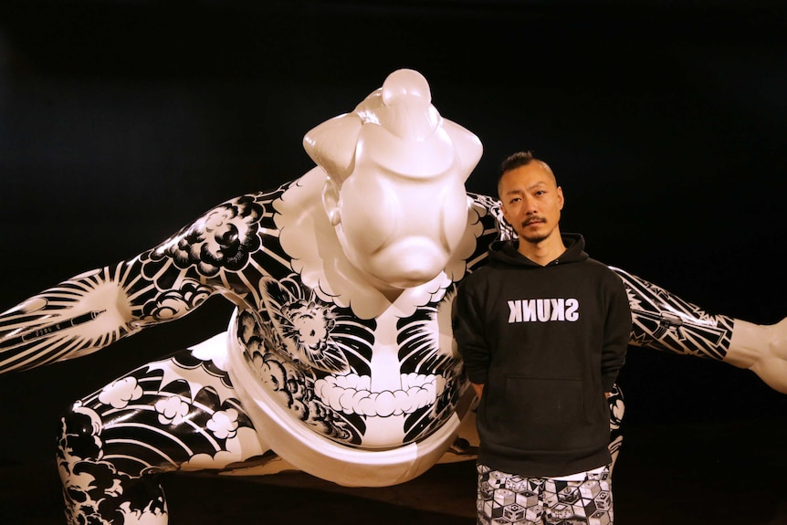 The artist poses with a larger than life sculpture of a sumo wrestler covered in tattoos