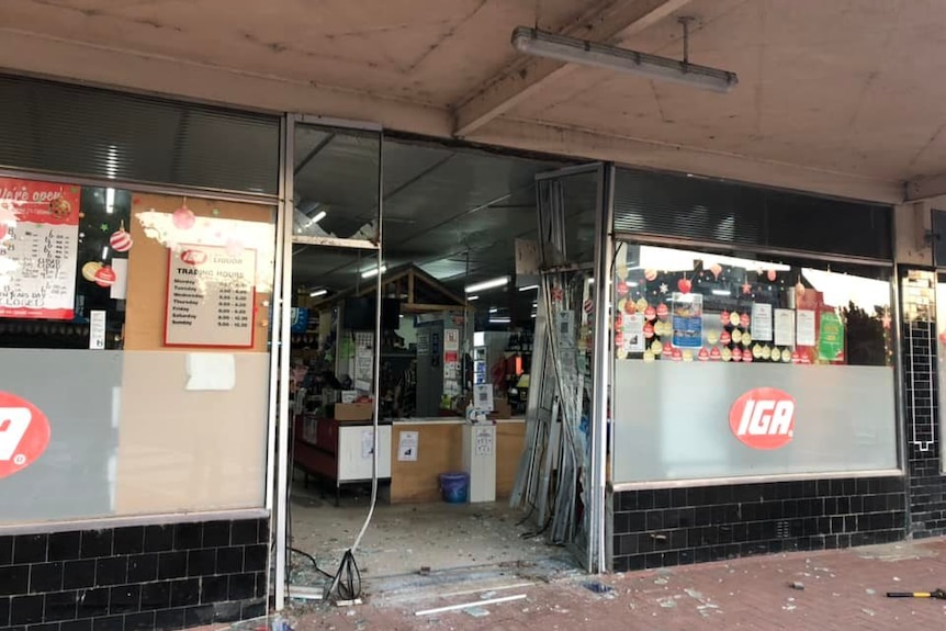 The entrance to an IGA supermarket with its door smashed in.