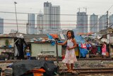 A little girl stands on train tracks near slums with skyscrapers in the background