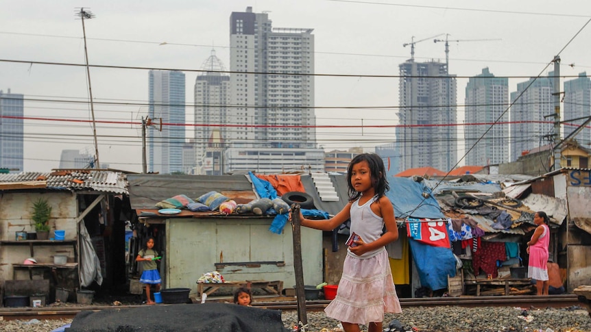 A little girl stands on train tracks near slums with skyscrapers in the background