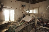 A dead body on a hospital operating table, buried under rubble.